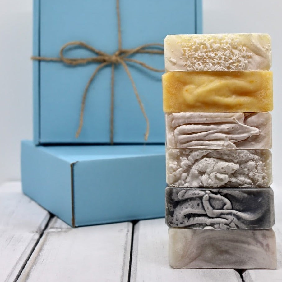 A stack of six artisan soap bars displayed in front of 2 blue gift boxes