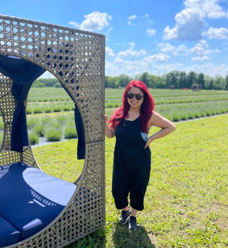 Genevieve, dressed in black overalls, standing by a lounger in front of lavender field