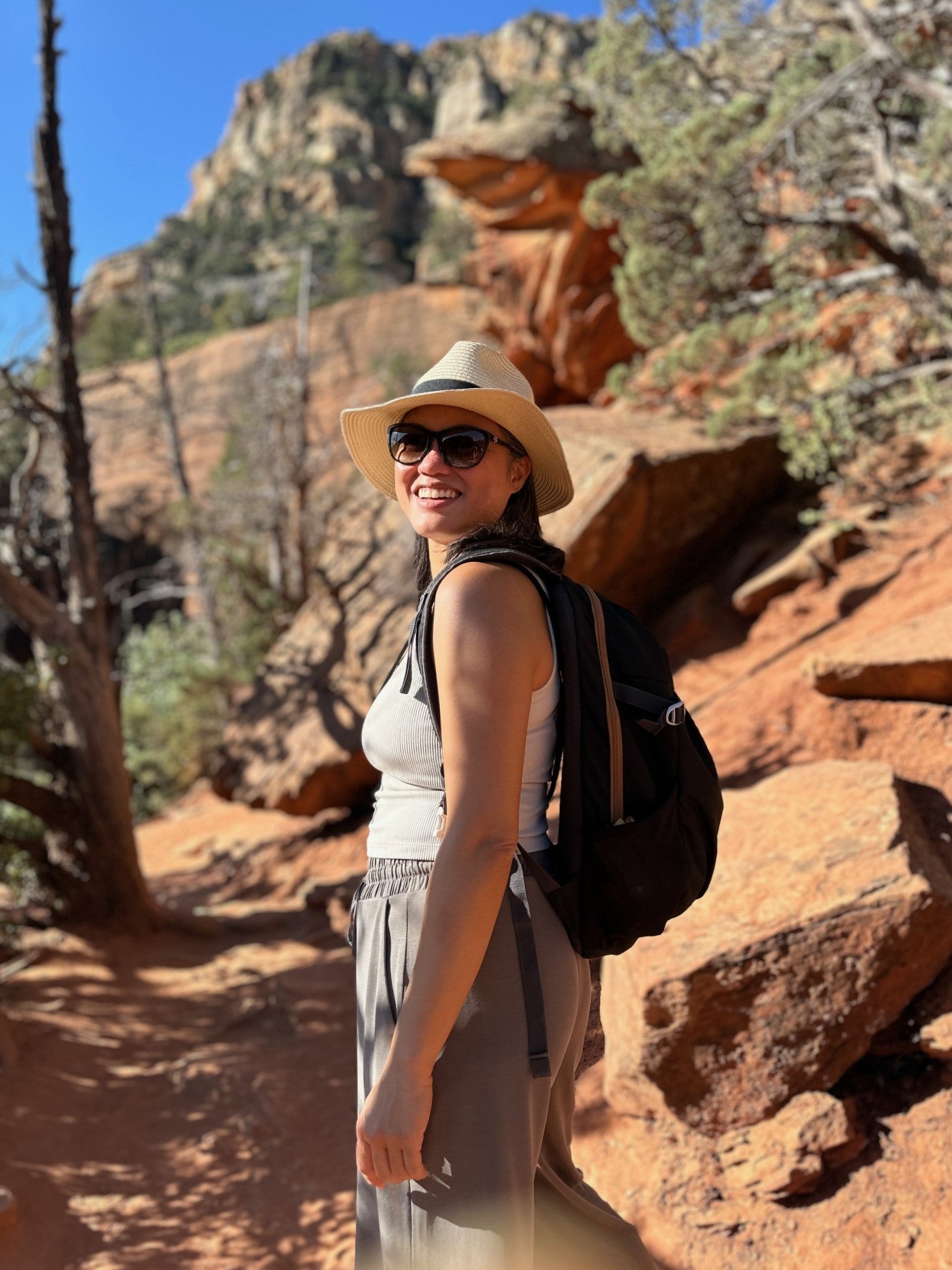 Leslie Tan in neutral colored clothing and a brimmed hat, wearing a black back pack, hiking in Sedona, Arizona