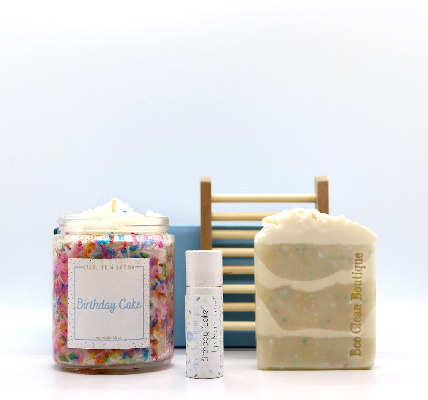 Colourful birthday cake candle, lip balm and artisan bar soap displayed in front of a ladder-style soap dish and blue gift box