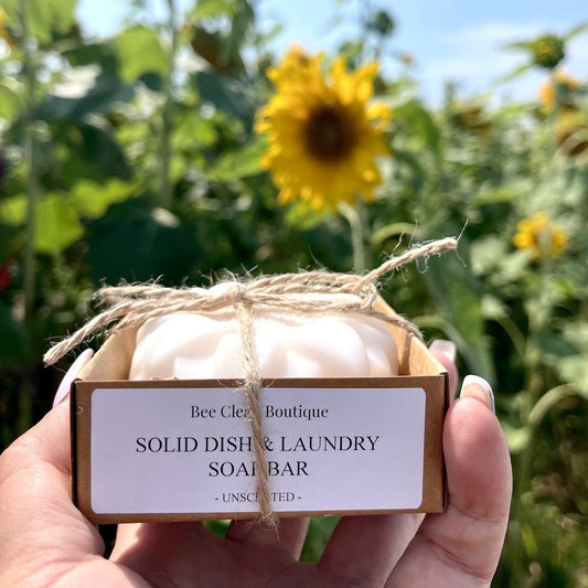 Solid dish and laundry soap bar in a kraft box tied with string, held up in front of sunflowers