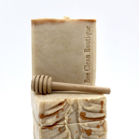 A handmade bar of goat milk and honey soap is displayed on a stack of soap; and a honey dipper is in front of the feature soap