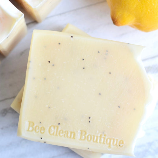 a stack of 2 lemon poppy seed bars of handmade soap is displayed on a marble counter with a lemon showing in the corner