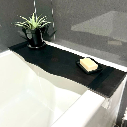 a black wooden bath caddy with a plant and bar of soap is on display over a bathtub in a bathroom