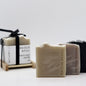 3 bars of loose bar soaps displayed in front of a set of soaps tied together with black ribbon on a wooden soap dish