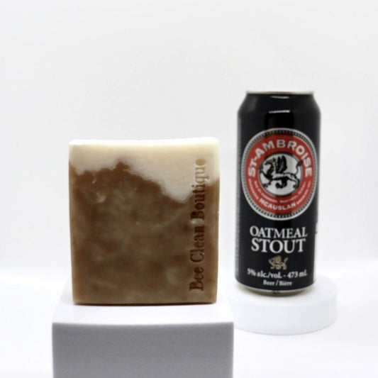 A bar of oatmeal stout artisanal soap is displayed in front of a can of oatmeal stout