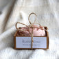 pink rose-shaped soap bar in a kraft box tied up with string on a white textured platform