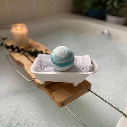 a bath bomb inside a bath tub-shaped holder on a bath caddy over a bathtub filled with bubbly water