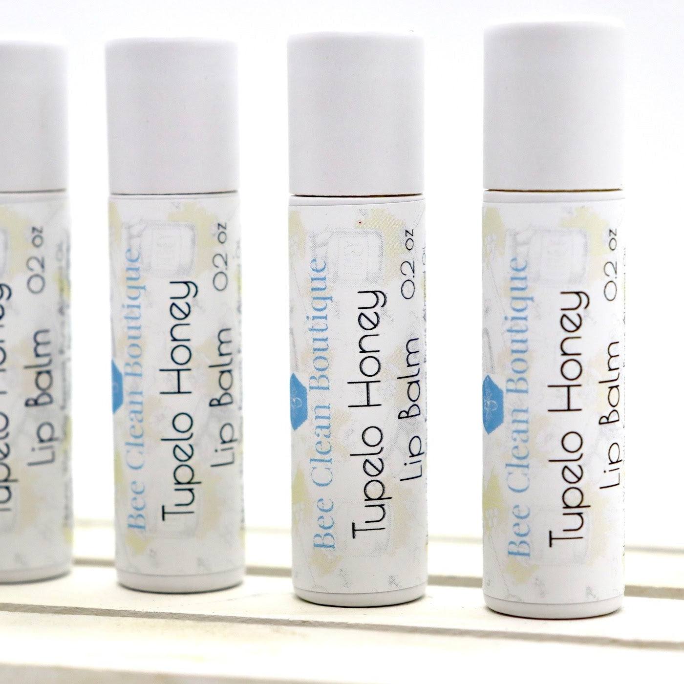 Four small tubes of Tupelo Honey flavoured lip balm standing on a wooden platform